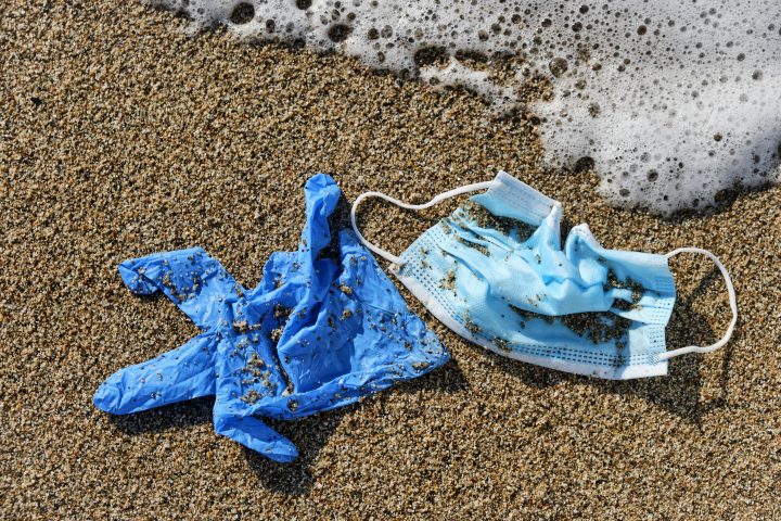 closeup of a blue used surgical mask and a blue latex glove thrown on the wet sand of the seashore of a beach